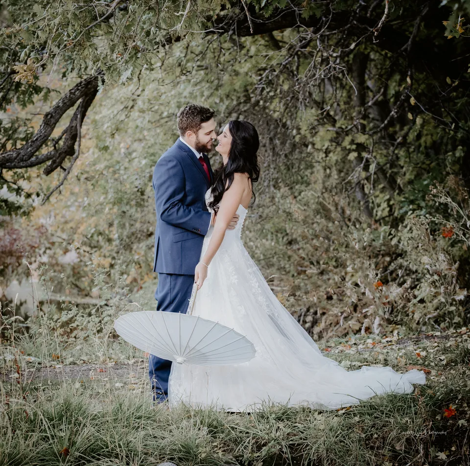 A bride and groom under autumn trees holding a white parasol